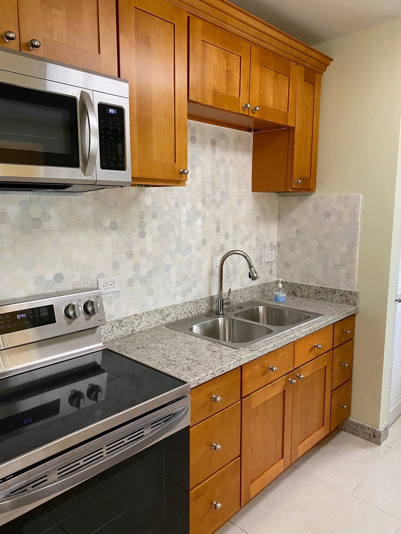 The kitchen after renovation, with granite counters, a marble backsplash and a three-seat bar