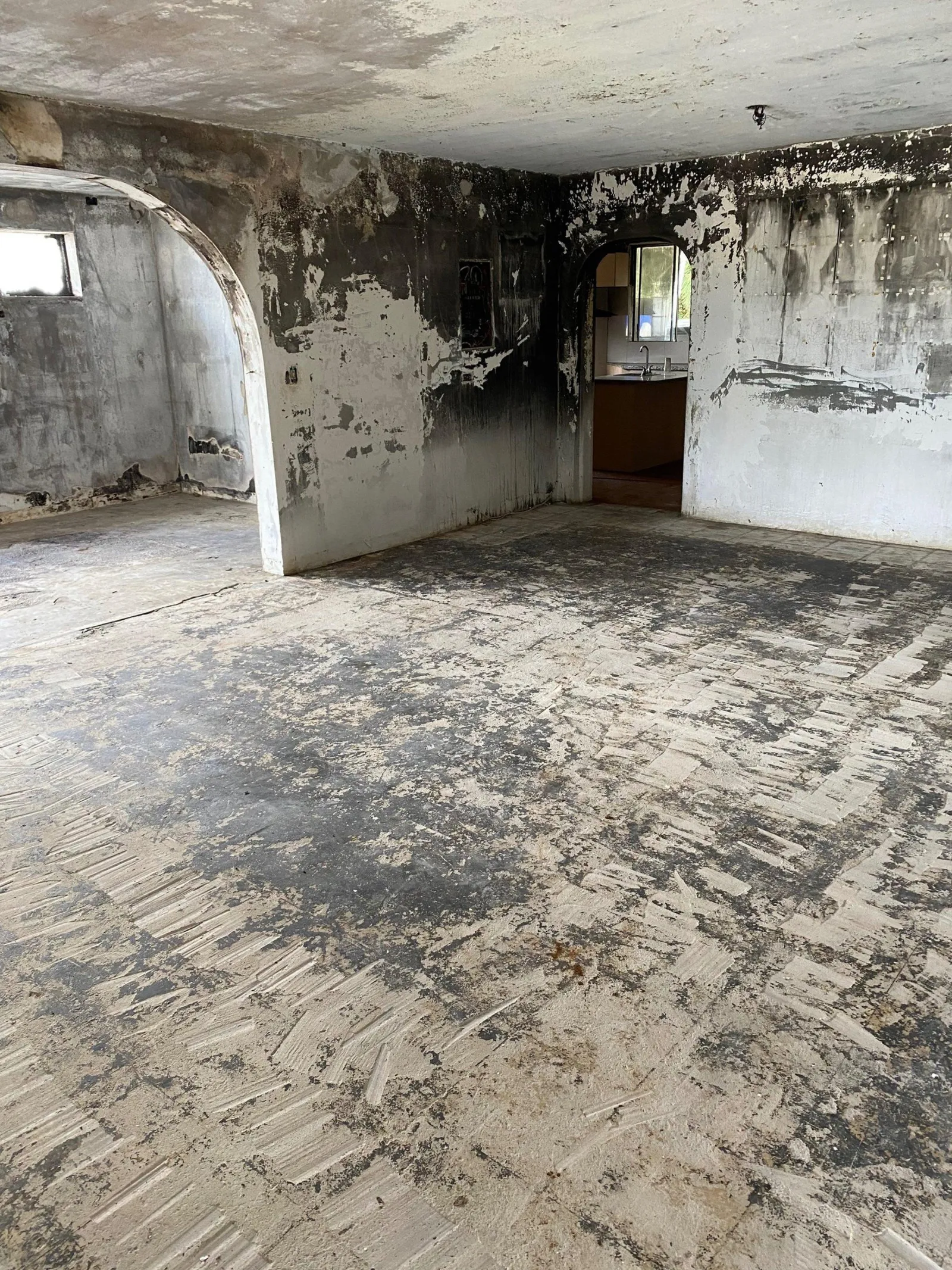 An open living area stripped back to bare concrete, walls blistered and the floor slab scraped clean