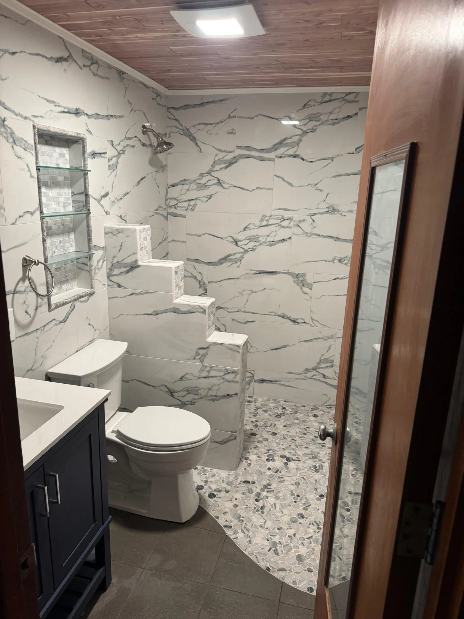 Finished bathroom with a cedar plank ceiling, a stepped shower bench and a pebble shower floor