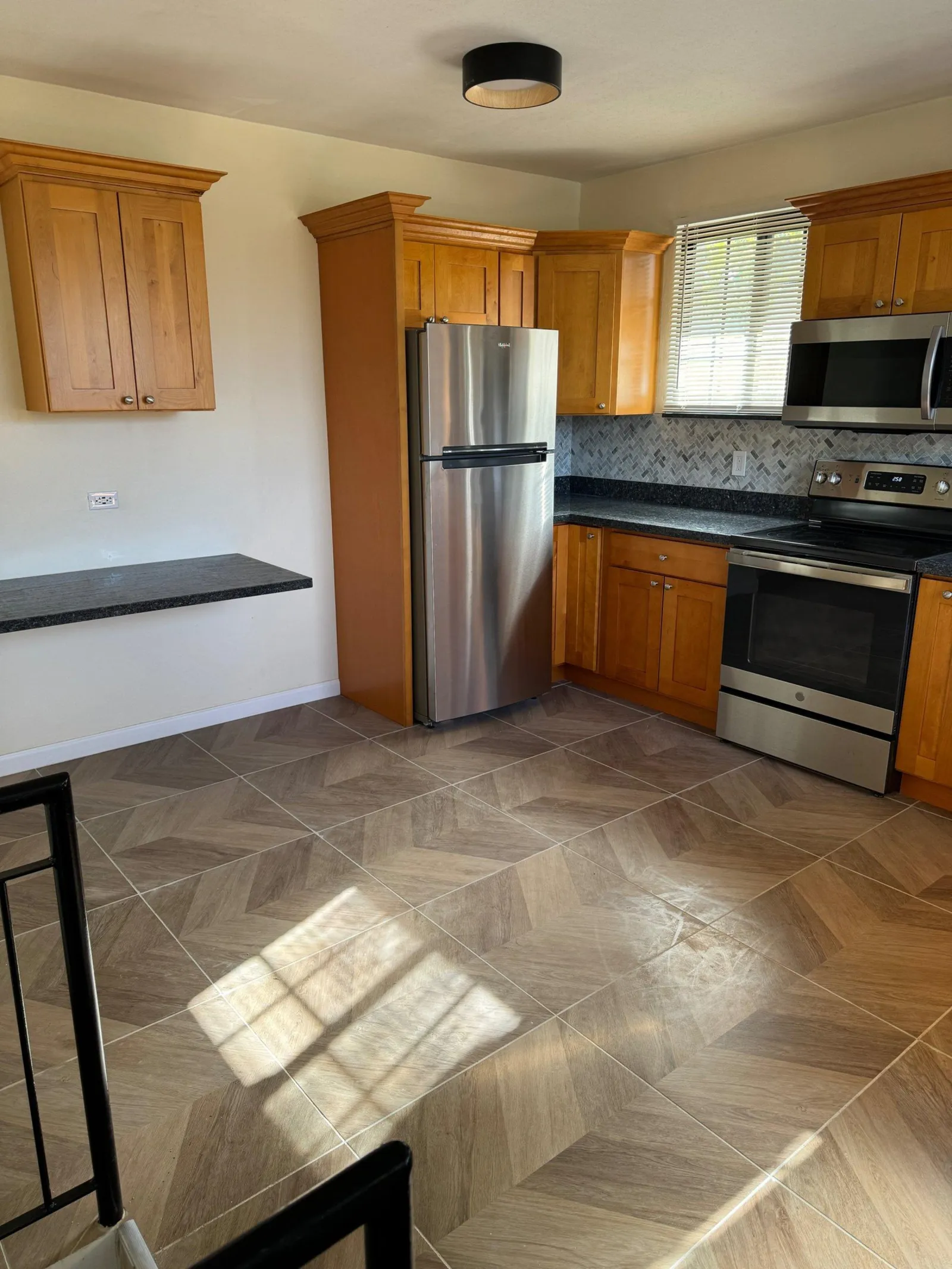 Finished kitchen with honey shaker cabinets, dark granite counters, a herringbone backsplash and stainless appliances