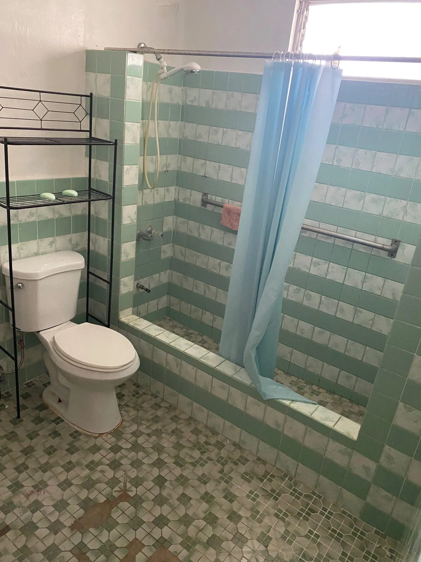 Bathroom with mint green striped wall tile, a mosaic floor and a blue shower curtain at the tub