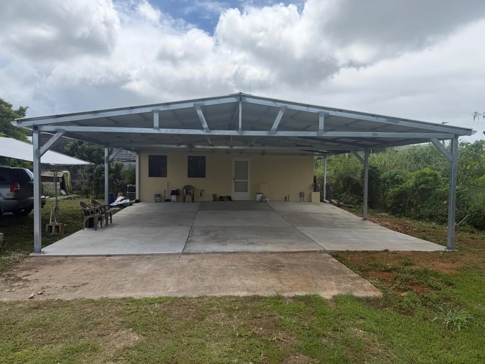 A galvanised steel gable carport with a metal roof over a wide new concrete pad