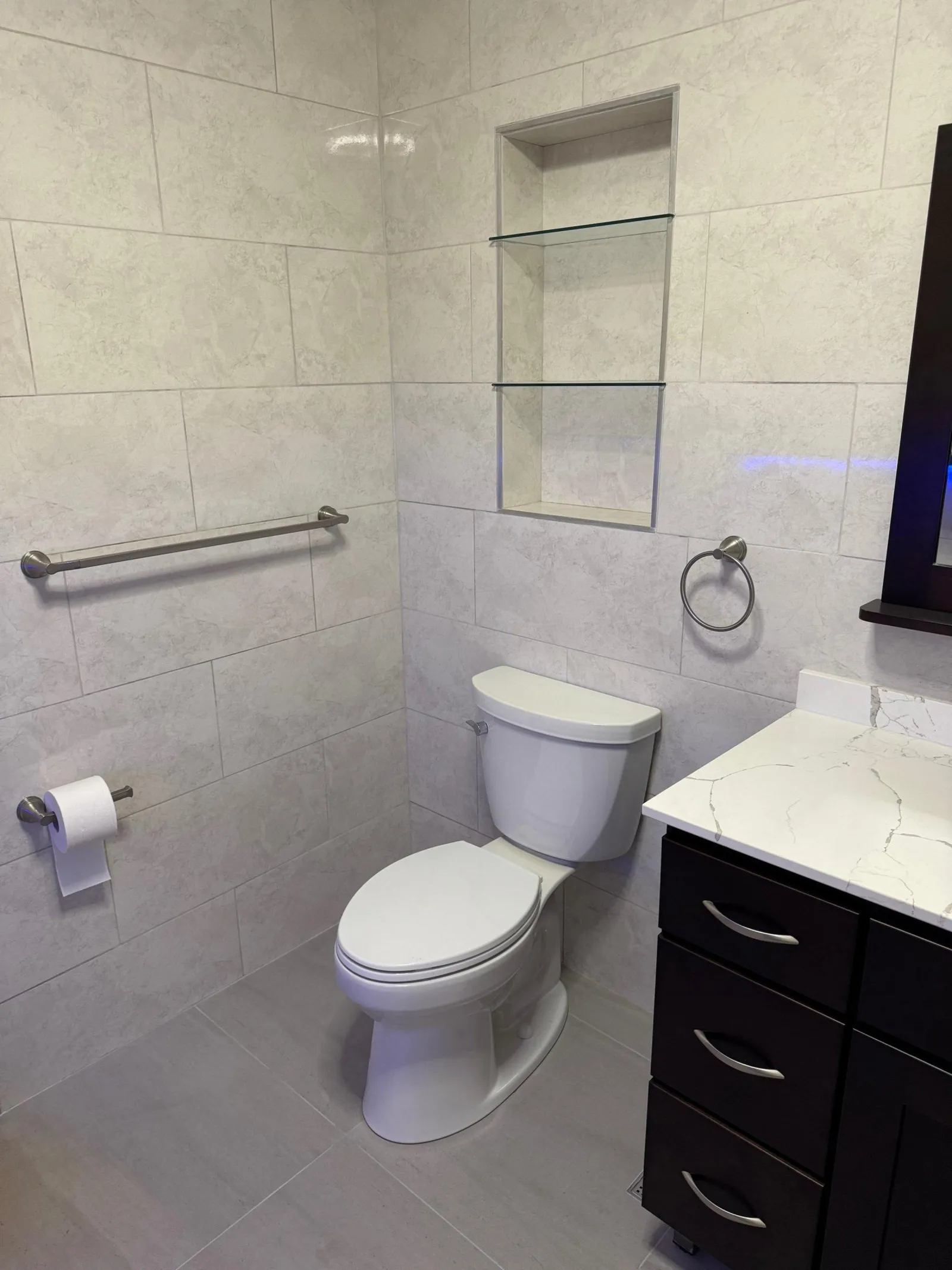 The same corner in white large-format porcelain, with a recessed glass-shelf niche and a dark vanity