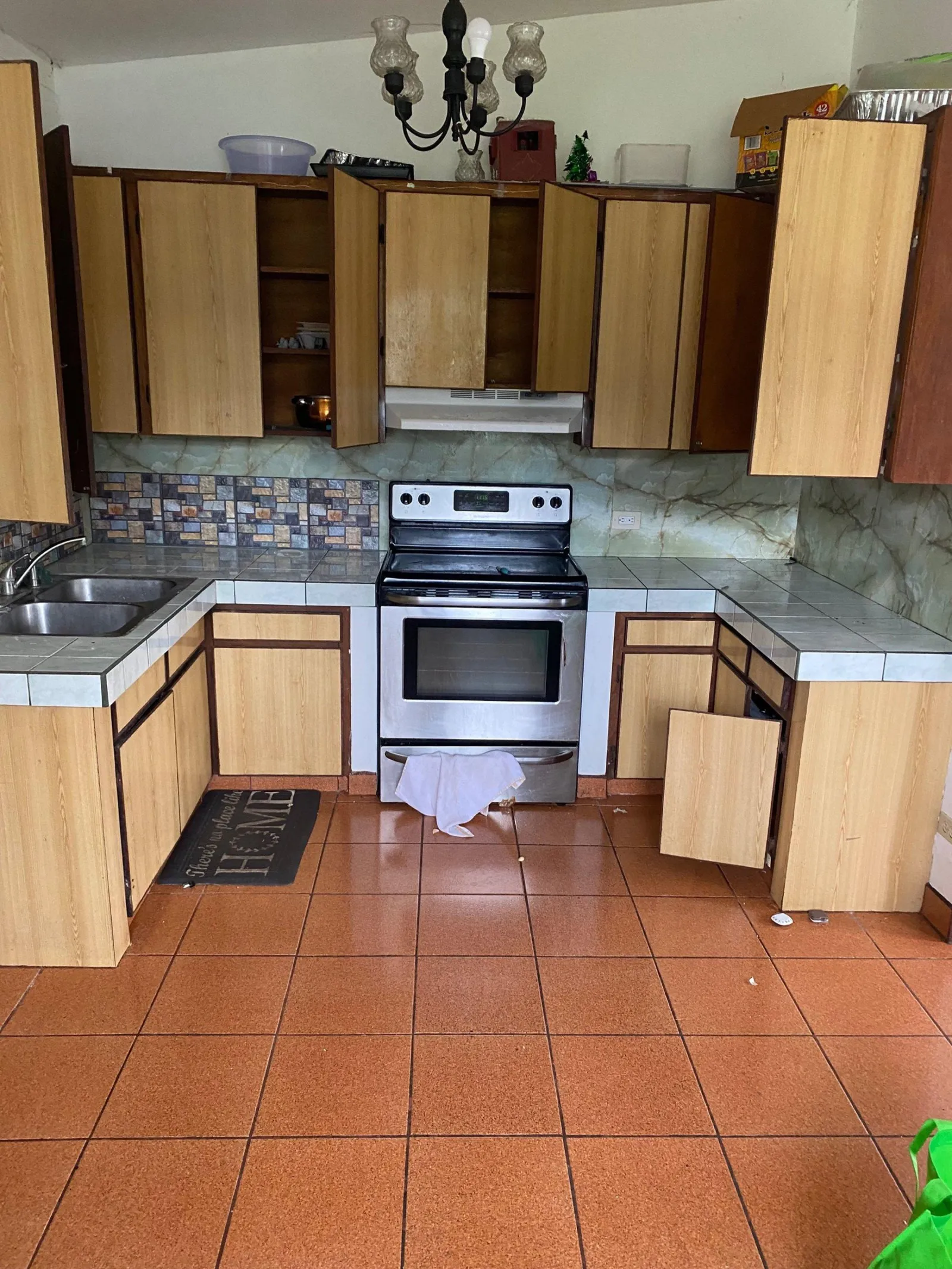 Dated kitchen with woodgrain cabinets, tile countertops and orange terracotta floor tile
