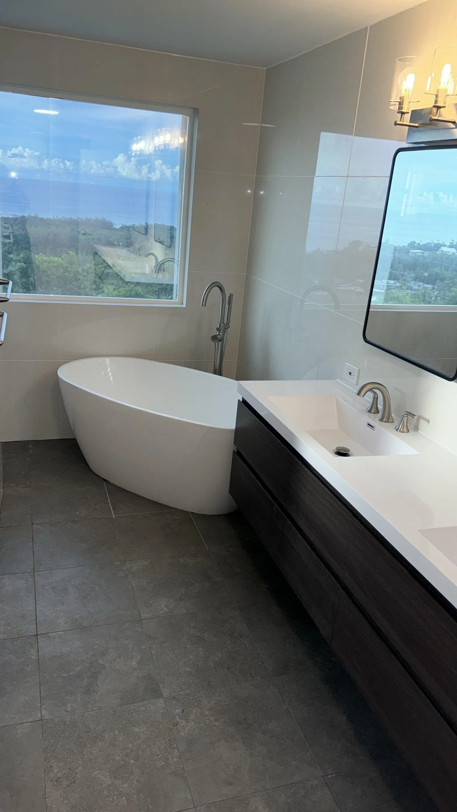 The finished room: a freestanding tub under the same window, beside a floating wood vanity
